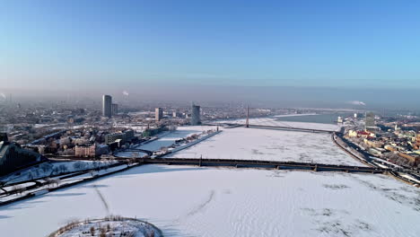 drone backwards shot over iced and snowy daugava river in riga city with bridges and buildings