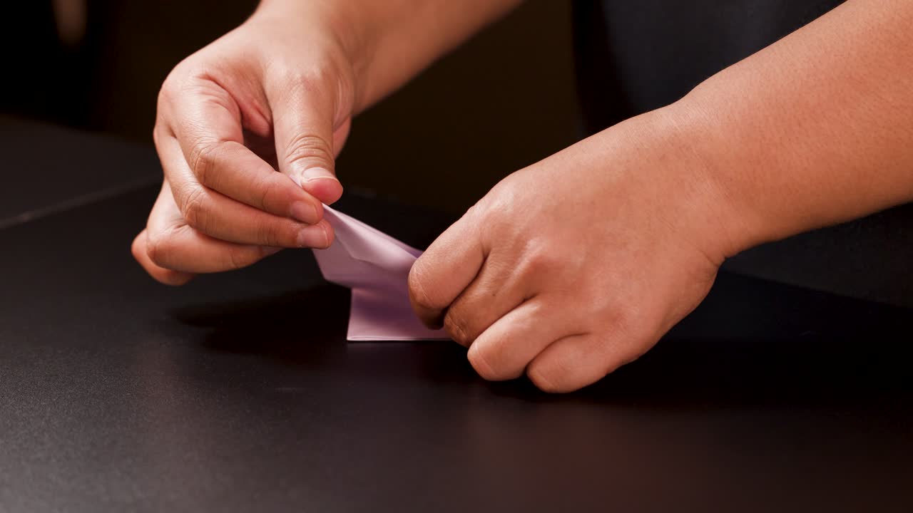 Person’s hands carefully fold white paper into an origami boat under soft, warm lighting