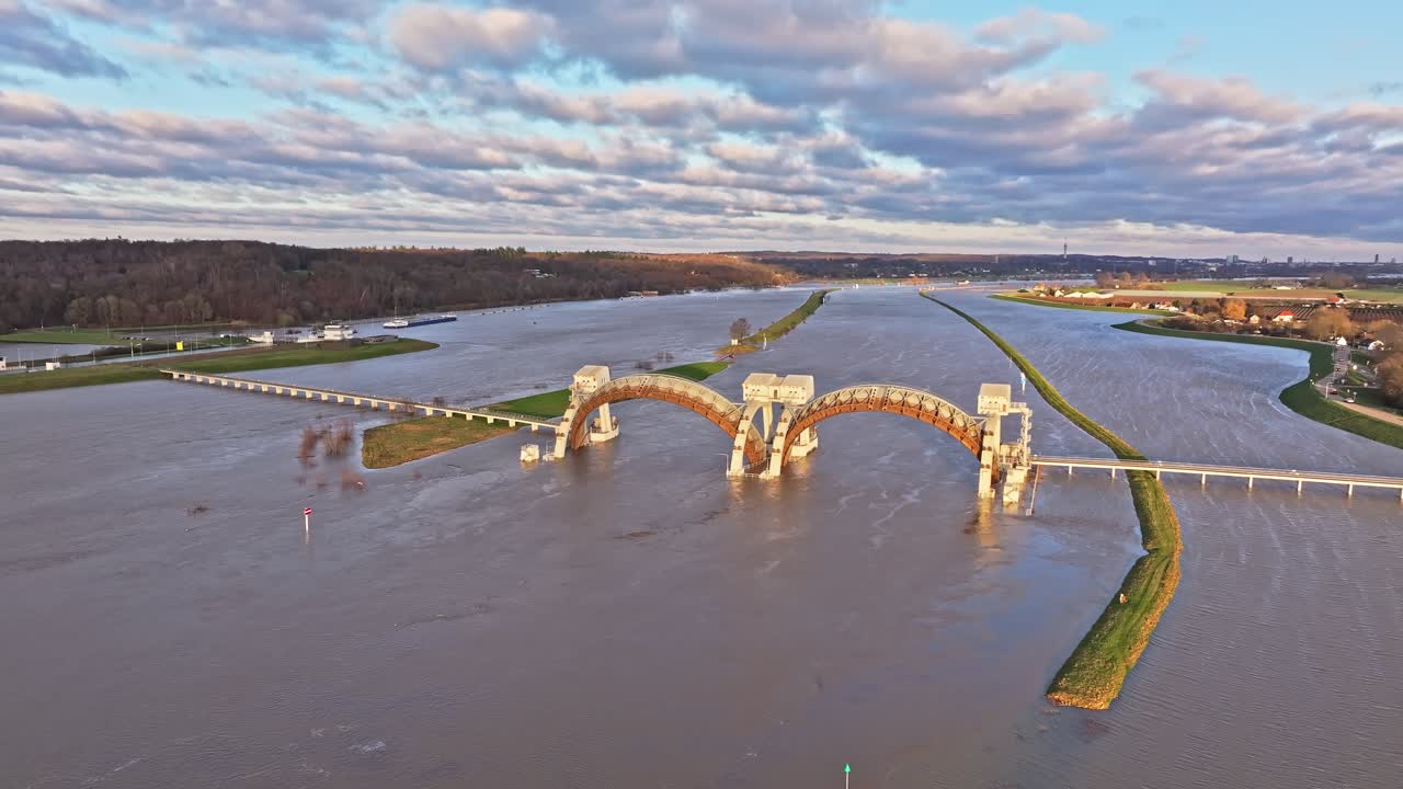 Right moving orbit drone shot at the weir of Driel during the sunset while the doors of the weir are open during high waterlevels