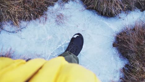 Persons-Feet-Stepping-On-Frozen-Swamp-With-Cracking-Ice-During-Winter-In-Norway