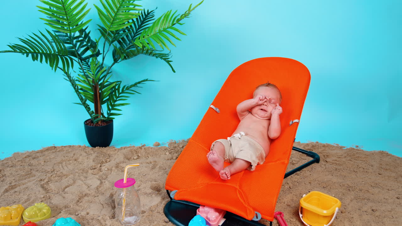 Happy little infant stretching in the orange baby chair. Newborn kid resting on the imitated beach.