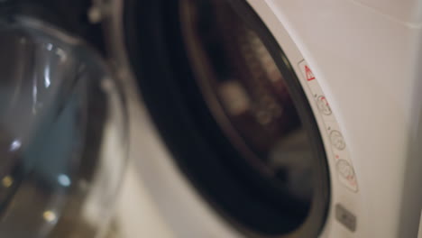 hand of a lady in pink shirt opening the door of a modern washing machine in a store, caution signs are visible on the machine with a blurred view of the hand touching the appliance