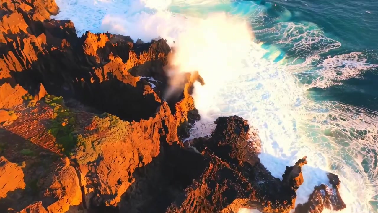 Vista aerea di potenti onde oceaniche che si infrangono contro una costa frastagliata all'ora d'oro