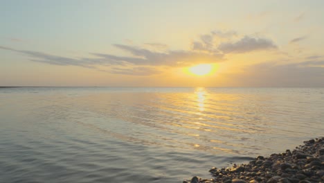 Pan-across-to-glistening-pebble-bank-with-calm-sea-during-sunset-in-slow-motion-at-Fleetwood,-Lancashire,-UK