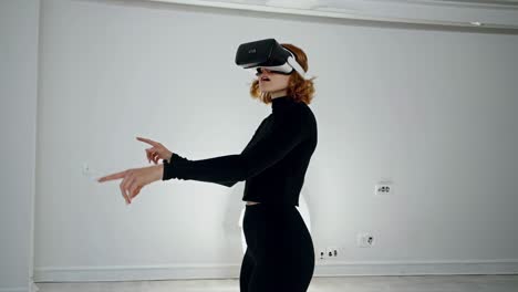 a woman in black using vr goggles, pointing in a modern white room