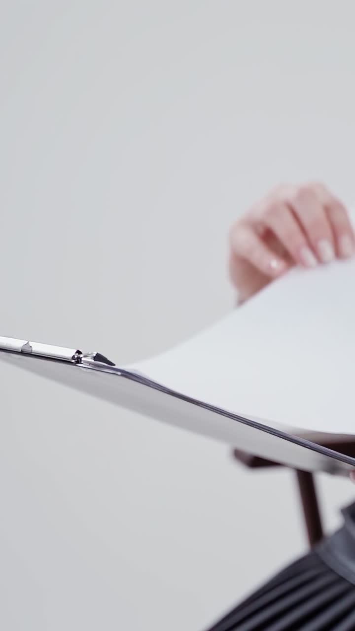 Folder with papers in woman's hands. Businesswoman in white blouse sitting in the chair and reading. Close-up. Slow motion. Vertical video