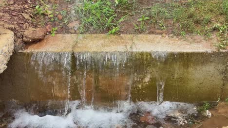 clean groundwater from the borewell flows over a small concrete barrier and continues into the nearby gutter. the gentle cascade and natural overflow
