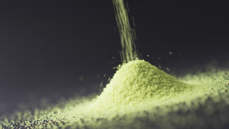 video of close up of green sand grains pouring into heap and copy space on black background