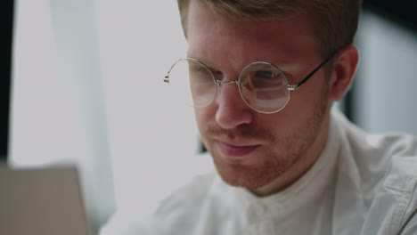 hombre guapo con gafas está leyendo noticias en la pantalla de la computadora portátil en la oficina, vista de cerca de la cara, abogado o empresario