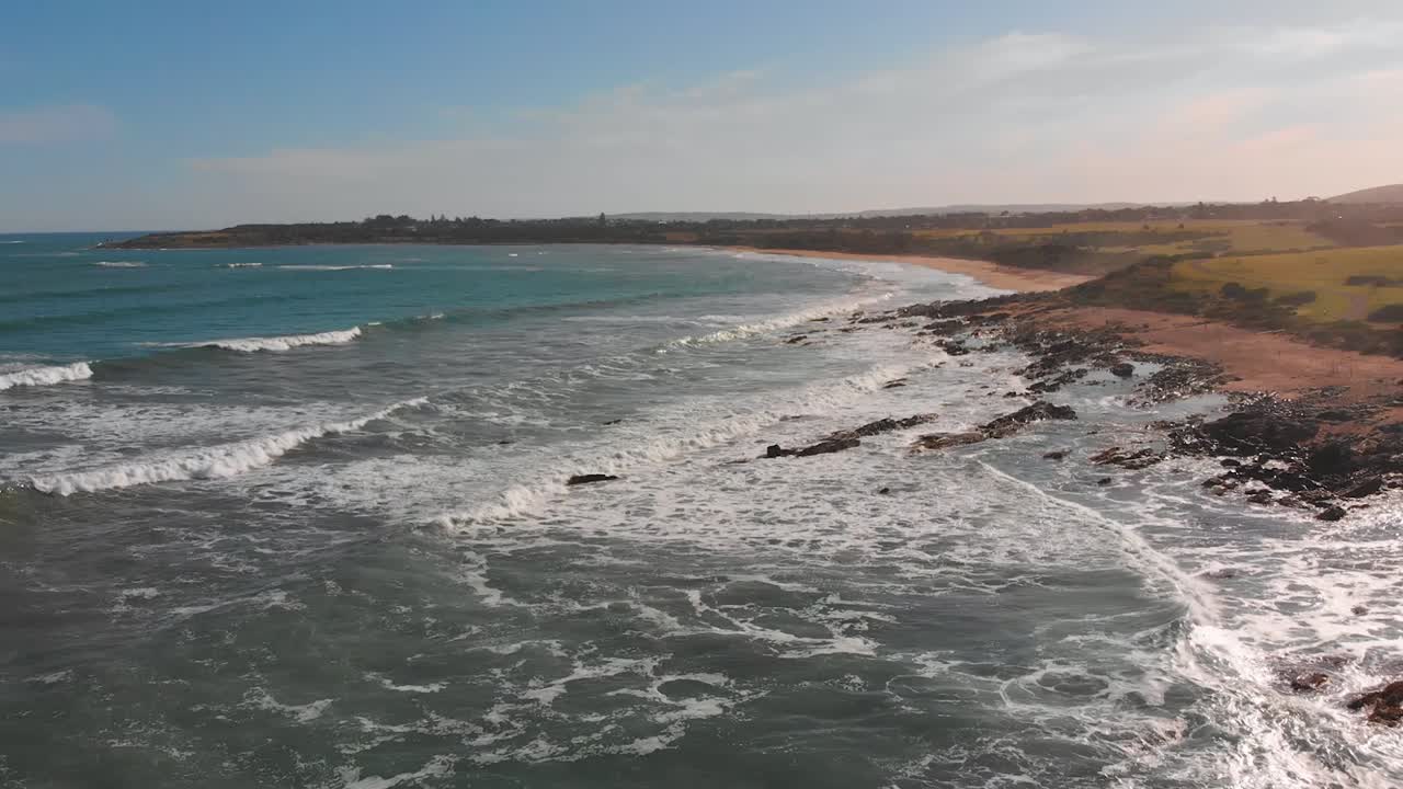 vista aérea cinematográfica de drones volando sobre las olas que se estrellan contra las rocas en una playa en middleton, australia del sur