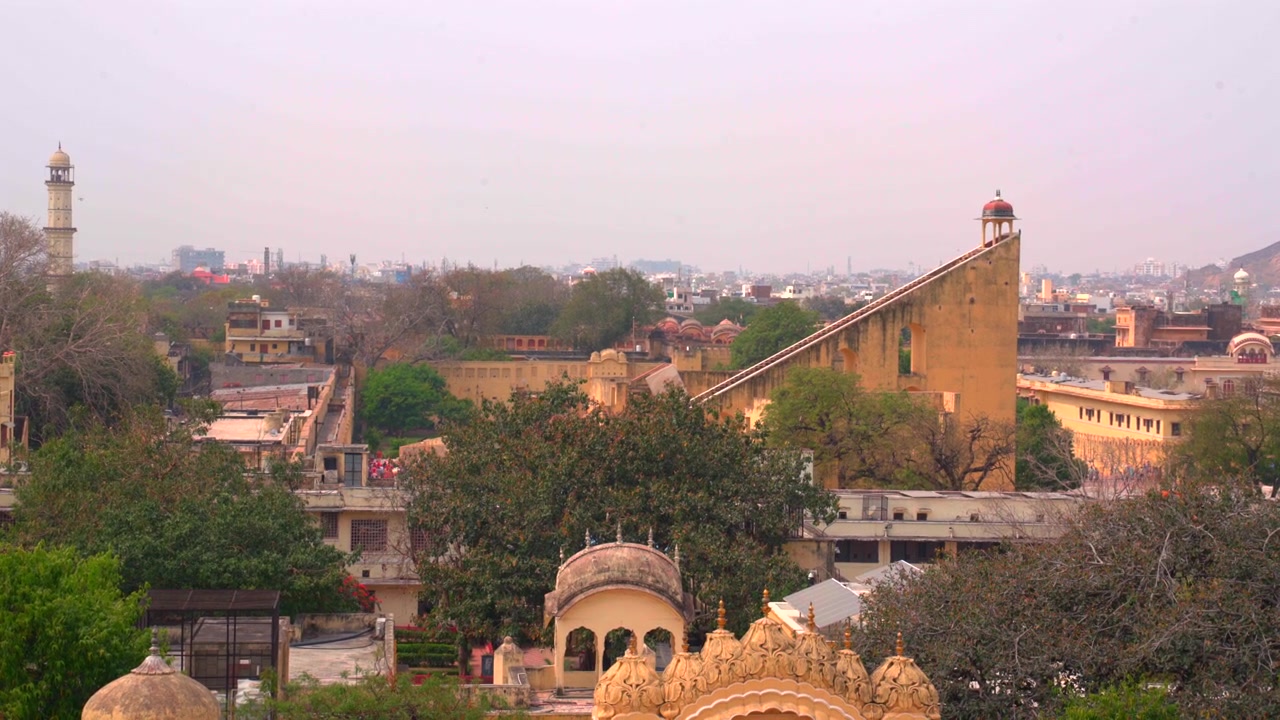Un'ampia inquadratura statica dello skyline dell'osservatorio Jantar Mantar a Jaipur, con l'enorme meridiana Vrihat Samrat Yantra e la storica torre Isar Lat sullo sfondo della città