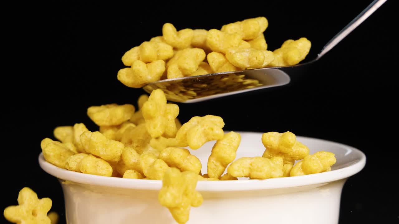 Star-shaped cereal in a bowl with spoon interaction against a black background, highlighting texture and movement