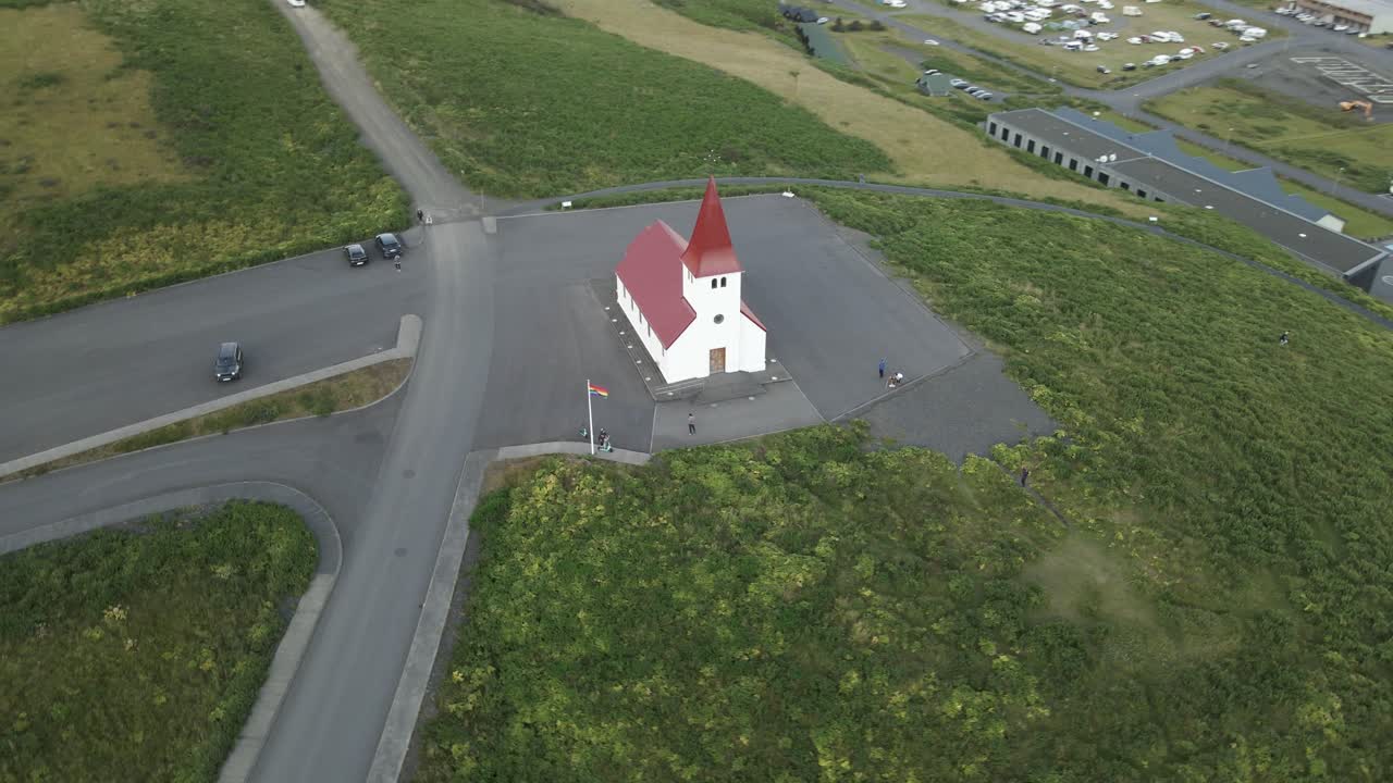 Bask in the ethereal glow of sunset with a captivating aerial view of the iconic white church in Vik, Iceland, perched atop a hill overseeing the town's tranquil panorama