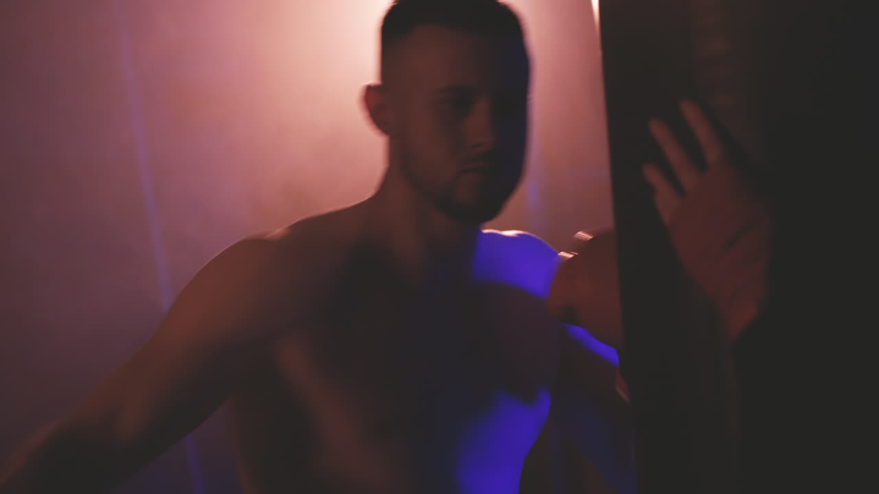 셔츠를 입지 않은 권투 선수가 복싱 백을 펀칭하여 워밍업