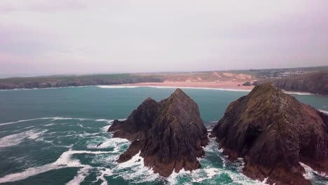 flyover drone-shot of a rocky island in the middle of the sea revealing the sandy beach in the background