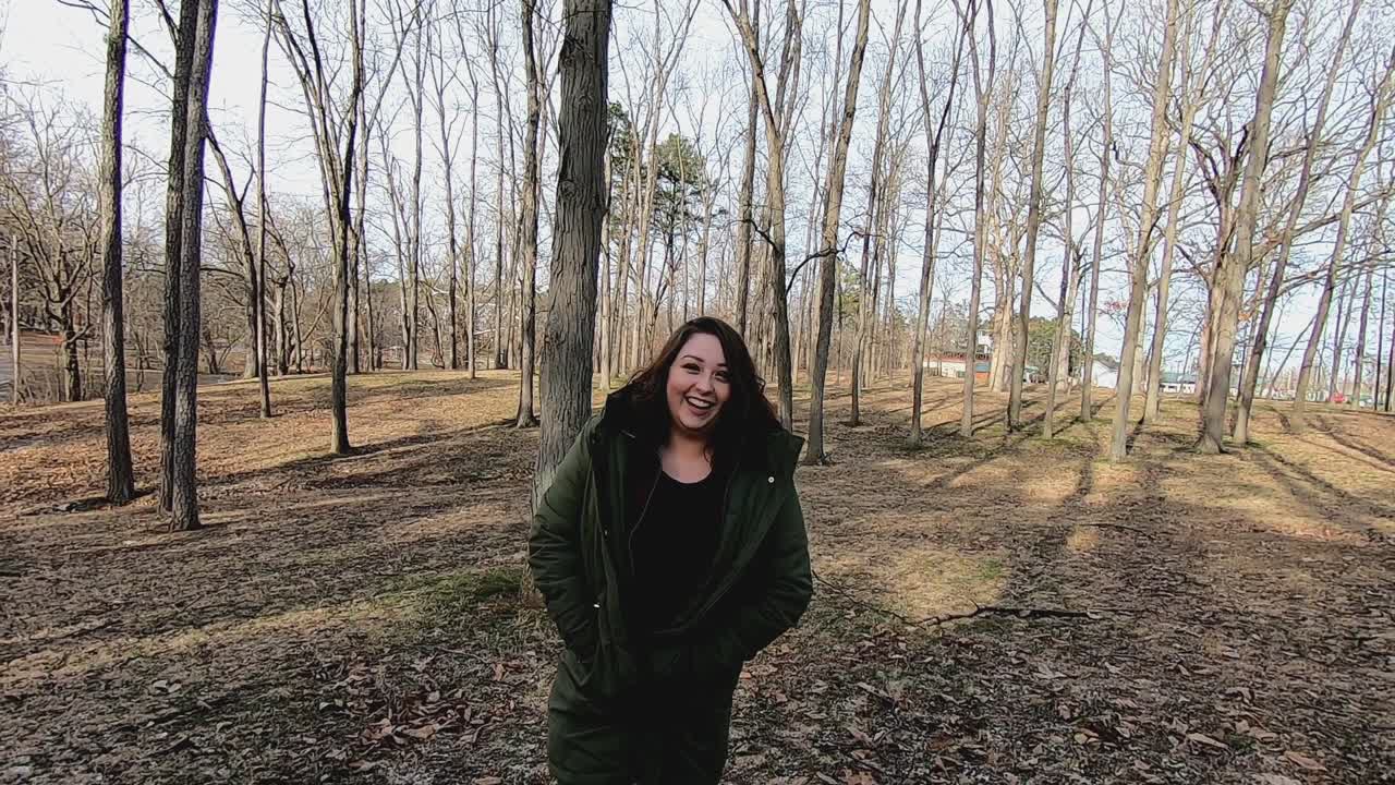 una joven y bonita mujer adolescente caminando por el parque riéndose y sacudiendo la cabeza mientras usa un abrigo verde