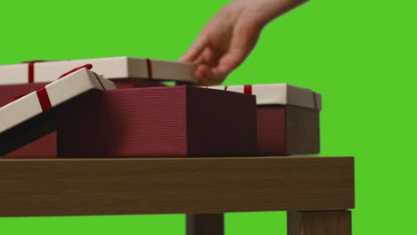 close up of man putting present into gift wrapped box on table shot against green screen 1