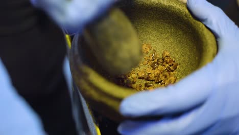 Close-up-shot-of-hands-grinding-palm-kernel-fruit-shells-with-mortar-and-pestle-or-pounder-into-smaller-pieces