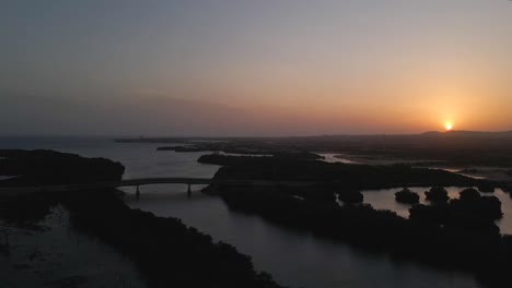 drone moves to the right gaining altitude revealing a silhouetted bridges, mangrove forests, ocean on the horizon and mountains with the majestic sunset, porlamar, margarita island, venezuela