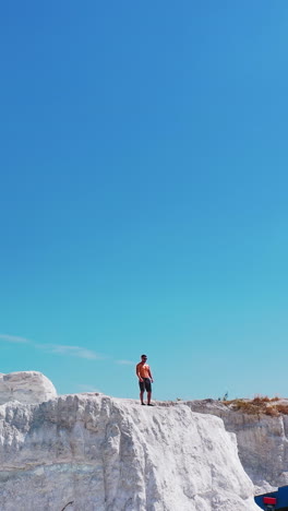 drone view on a sporty man in canyon. sportsman in shorts standing on the edge of the white hill in a bright summer day. aerial view. vertical video