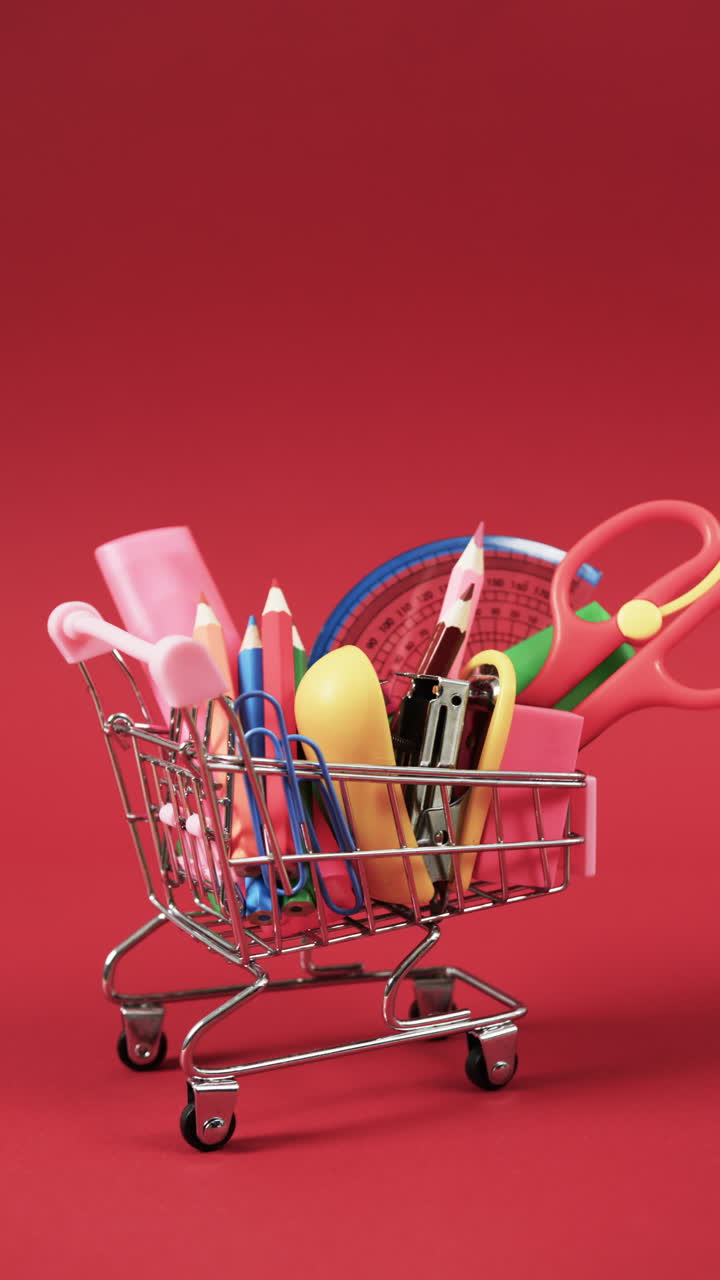 Vertical video of close up of shopping trolley with school items and copy space on red background