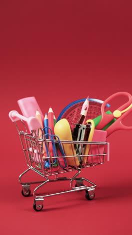 vertical video of close up of shopping trolley with school items and copy space on red background
