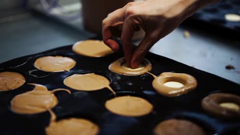 Close-up-shot-of-baker-filling-chocolate-mix-cupcakes,-inserting-white-chocolate-in-the-core-and-pressing-the-center-almost-overflowing-the-batter