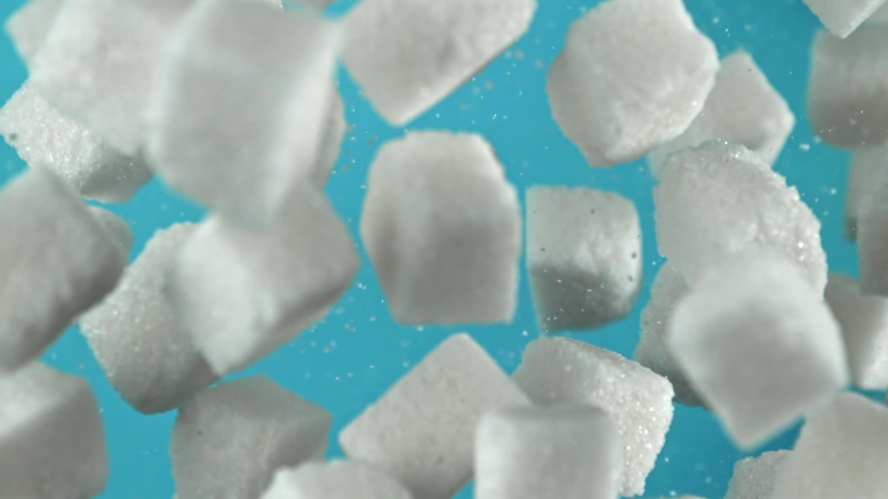 Terrones de azúcar blancos cayendo en cámara lenta sobre un fondo azul
