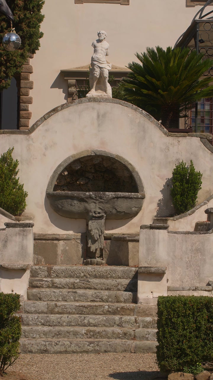 Scalinata in pietra e statua classica all'ingresso della villa con siepi potate alla luce del sole