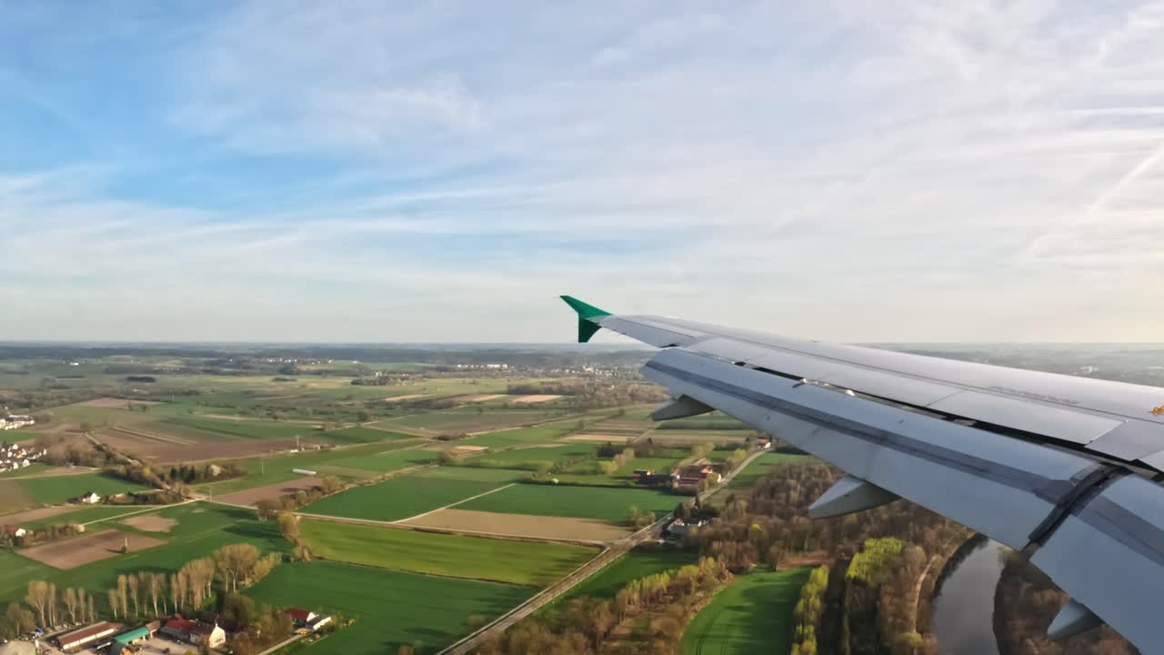 View from airplane window during landing approach to Munich Airport, showing extended flaps and green fields below, captured with specific camera settings