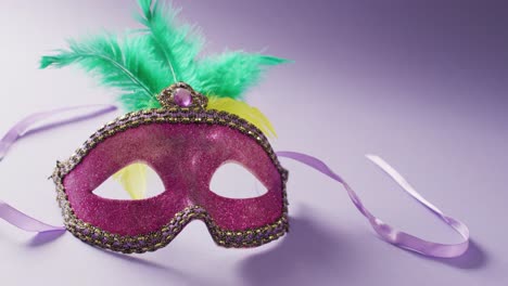 video of pink carnival masquerade mask with green feathers on lilac background