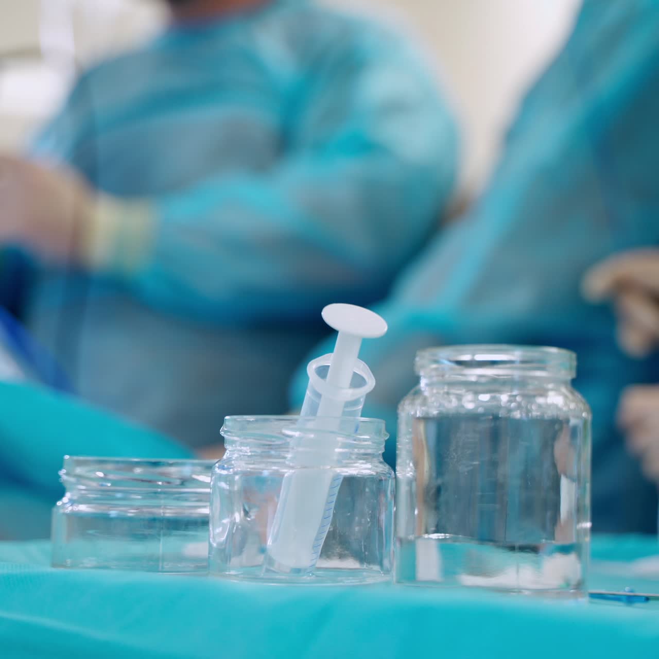 Sterile surgical tools on table. Jars with balanced solution and syringe on blur background of medical specialists performing an operation. Close-up.