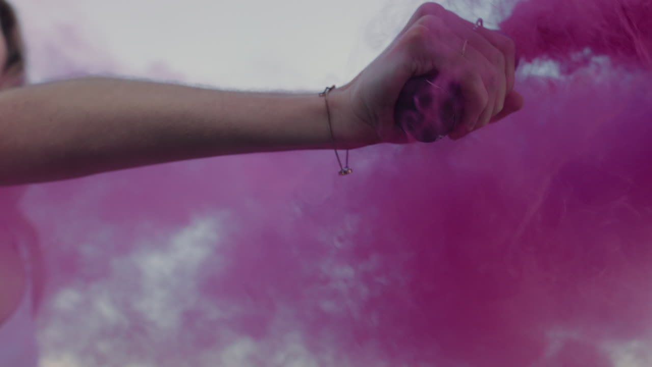 donna che tiene in mano una granata di fumo rosa che balla sulla spiaggia all'alba celebrando la libertà creativa