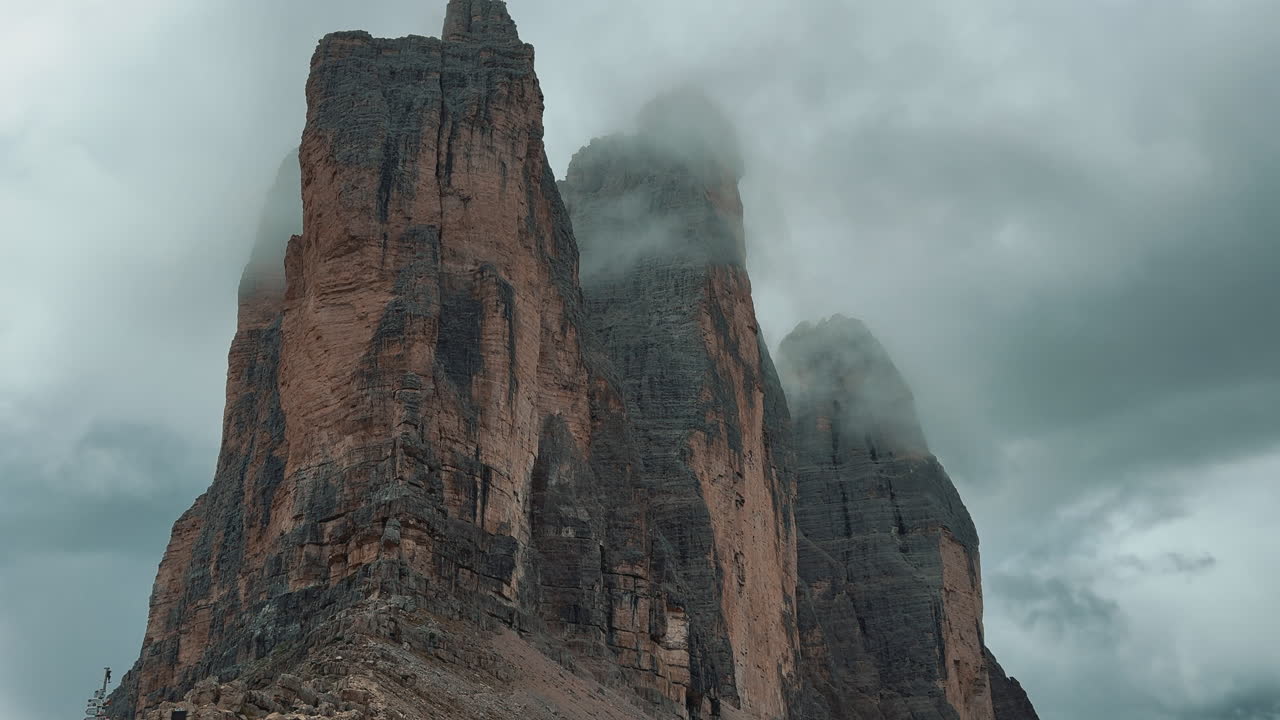Majestic Tre Cime di Lavaredo peaks rising through ethereal clouds, revealing dramatic Dolomites landscape in pristine Italian alpine wilderness