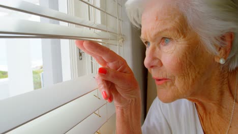 close-up of caucasian senior woman looking through window blinds at home 4k