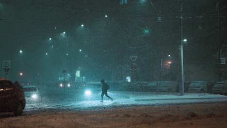 People-silhouettes-crossing-the-street,-cars-driving-on-a-frosty-winter-night-during-a-blizzard