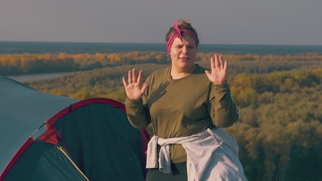 joyful plump girl dances with raised hands near blue tent