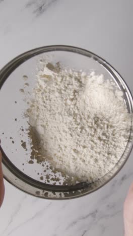 fotografía aérea vertical de la harina siendo tamizada en la superficie de trabajo de mármol para hornear