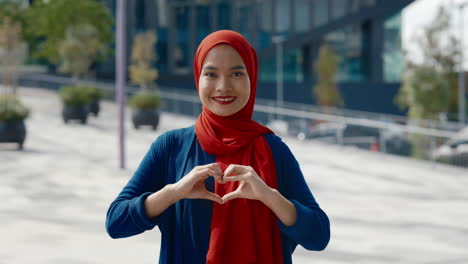 young woman in hijab makes heart shape with hands