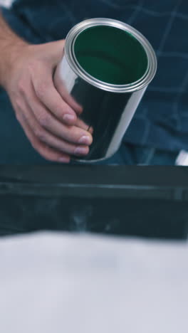 cu, dolly shot: man in blue shirt pours bright green paint into plastic tray on floor covered with foil in room closeup