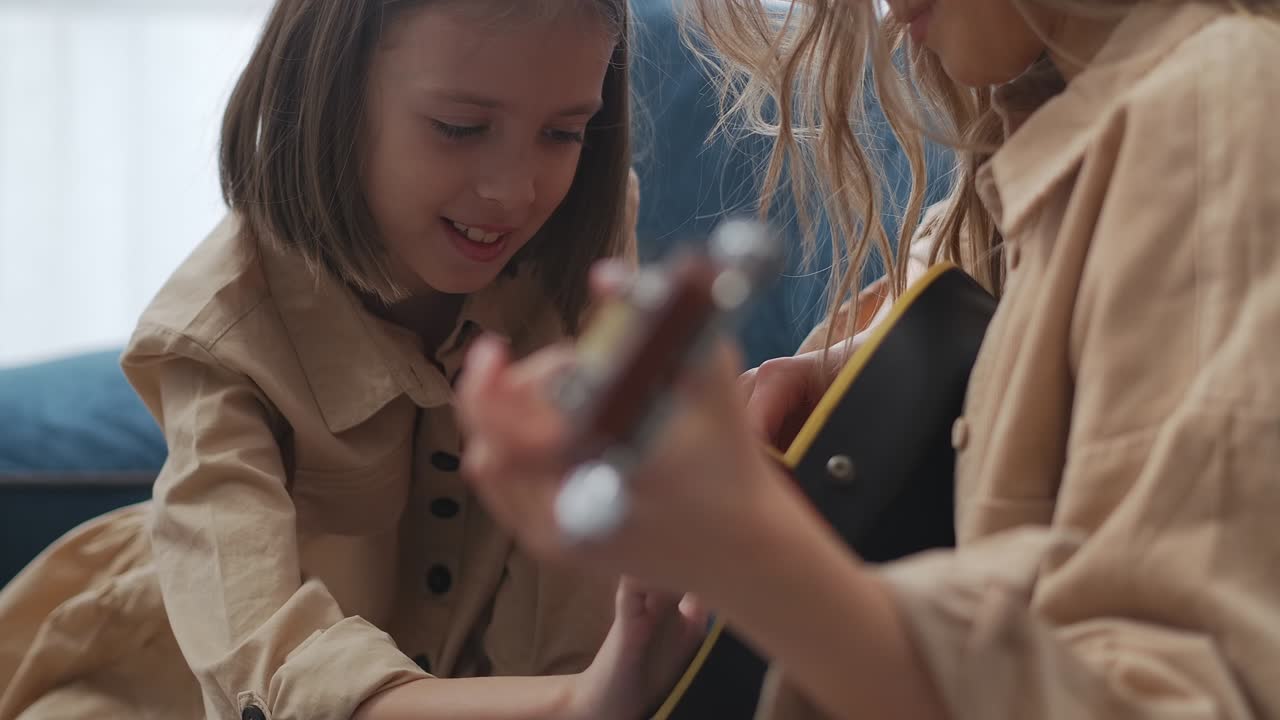 happy little girl is laughing when looking how her mother is playing guitar, portrait of smiling child