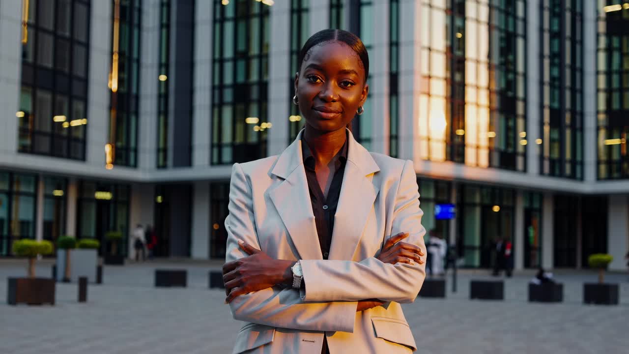 joven mujer de negocios se encuentra con confianza con los brazos cruzados frente a un moderno edificio de oficinas, exudando profesionalismo y éxito en el cálido resplandor del sol poniente