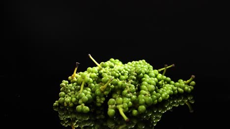 a cluster of fresh green peppercorns rotates smoothly on a reflective black surface, illuminated by dramatic studio lighting with a seamless, high-contrast look