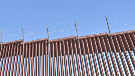 older man in front of border wall dividing united states and mexico, pointing and smoking cigar.