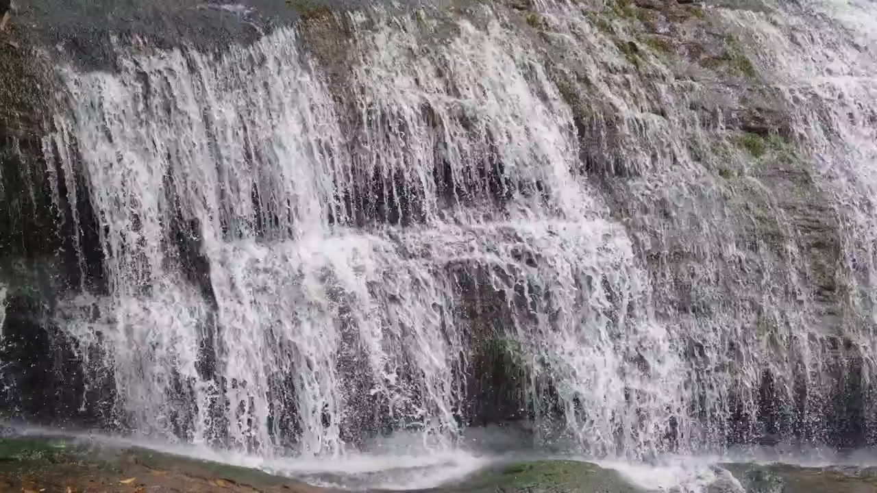 water cascade in Munnar, Kerala, with clear white water flowing rapidly over a rocky mountain slope, creating multiple layers of cascading waterfalls. The close-up view focuses on the powerful flow