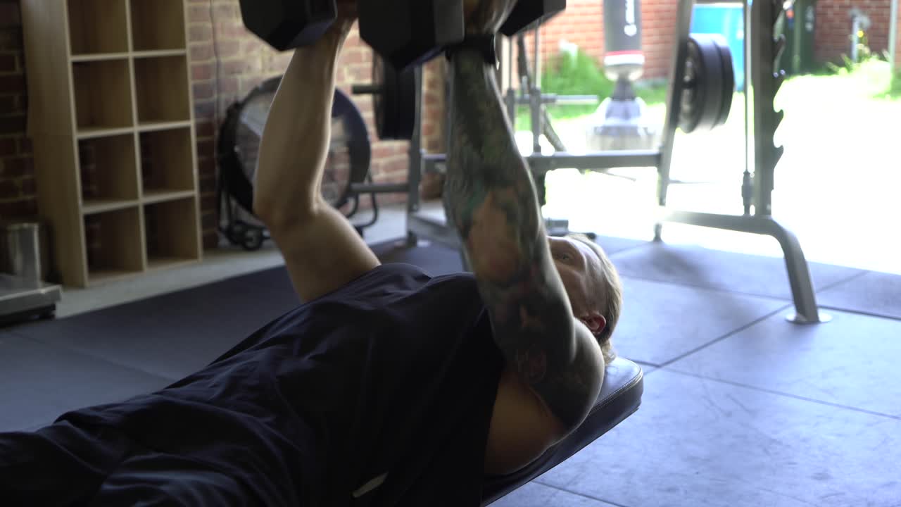 Tattooed man in home gym close up doing close grip dumbbell bench press