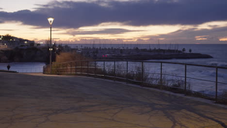 Straße-Entlang-Der-Meeresseite-Mit-Baumschatten,-Die-Während-Des-Frühen-Sonnenaufgangs-Vom-Lichtpfosten-Geworfen-Werden,-Während-Ein-Unbekannter-Mann-In-Richtung-Geht