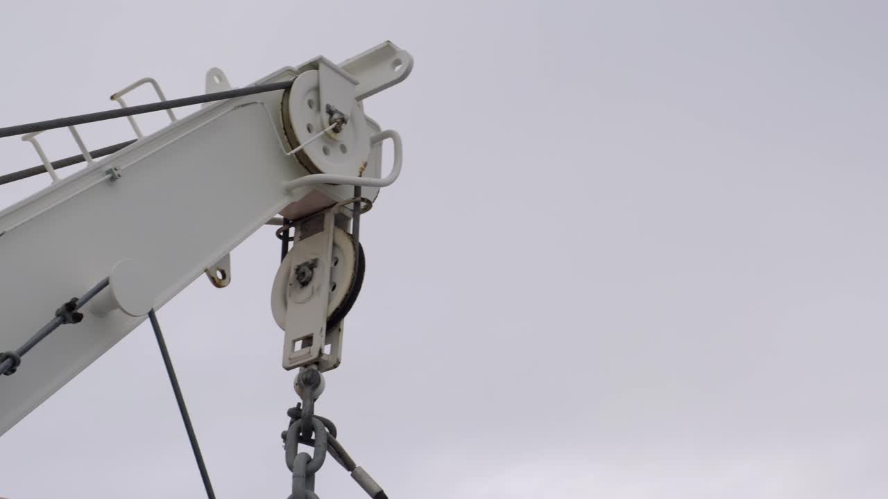 foque blanco del colgador de bote salvavidas con el bloque de gancho en la parte superior, visto desde un ángulo bajo contra el cielo nublado