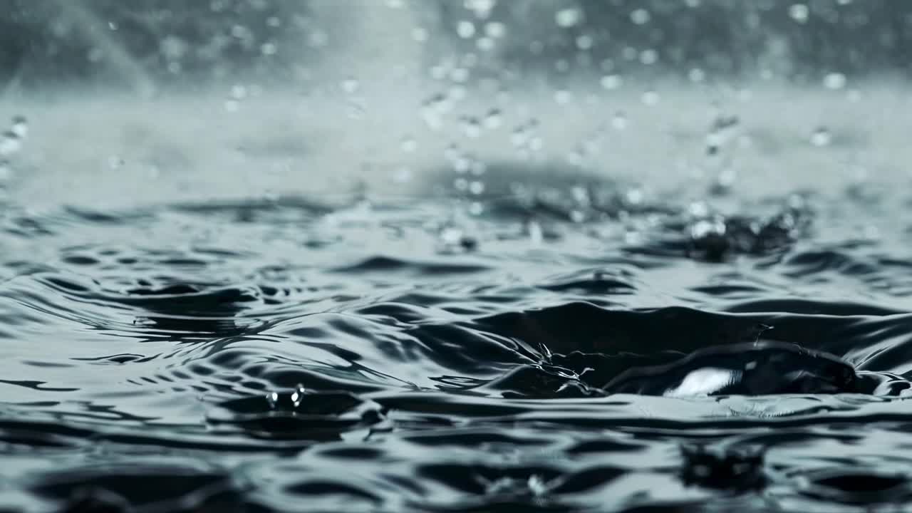 Close-up video of raindrops splashing on a surface, captured from a low angle