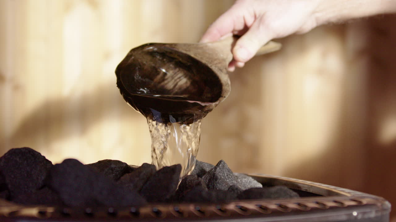 Water poured onto heated rocks of stove in wooden sauna, wellness ritual